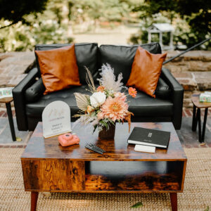 Black leather loveseat sofa staged with end tables and a coffee table. Accents added such as brown leather pillows and tabletop decor.