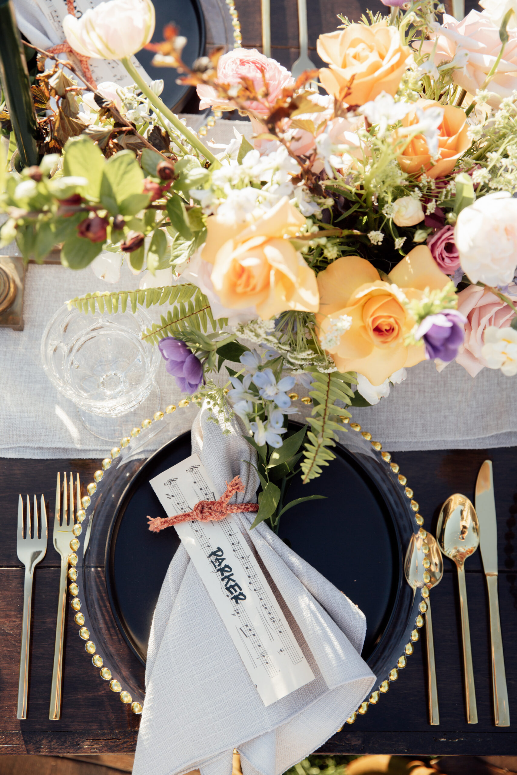 Image of tabletop setting using Gold beaded rim chargers, black stoneware plates, Primrose gold flatware, and clear vintage goblets