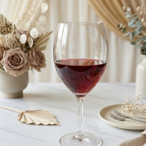Red wine glass staged on a wedding guest table with floral arrangements and other tabletop items
