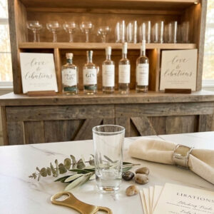 Double shot glass at a wedding on a bar during cocktail hour. Pictured with an assortment of alcohol and bar glasses.