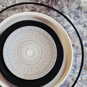 Black glass rim charger with sand stoneware dinner plate, black stoneware coupe salad plate, and cream and black accented b&b plate. All on a variety of brown-hued marbled linen.