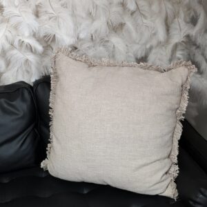 Tan throw pillow with fringed edging.